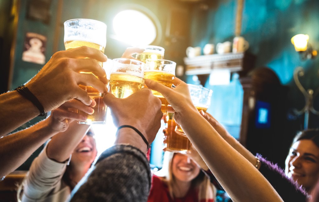 Group of happy friends toasting with beer in a vintage beer bar, focus on half pint glass